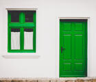 Eine grüne Tür und eine grünes Fenster eines weißen Hauses sind zu sehen. Man sieht nur einen Bildausschnitt. 