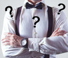 Der Oberkörper eines Mannes ist zu sehen, mit weißem Hemd, Hosenträgern und Fliege. Auf dem Bild sind 3 Fragezeichen. 