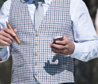 Ein Business Herr, welcher in der einen Hand ein Handy hat und in der anderen Hand einen Stift. Er trägt ein Krawatte und eine Weste. Man sieht nur den Oberkörper.